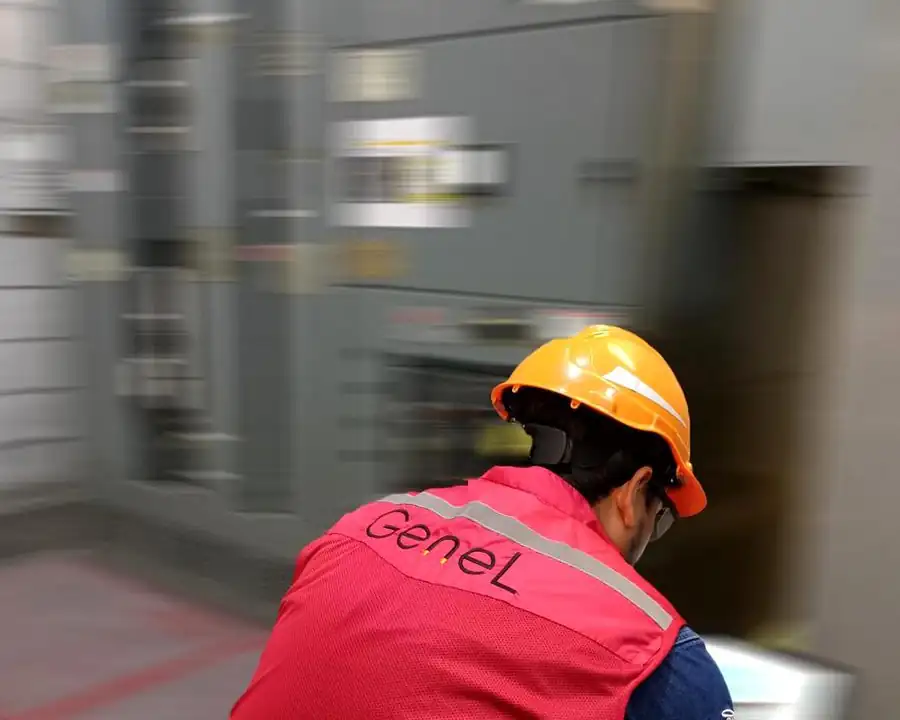 Técnico de GENEL con chaleco de la empresa trabajando frente a un tablero eléctrico industrial
